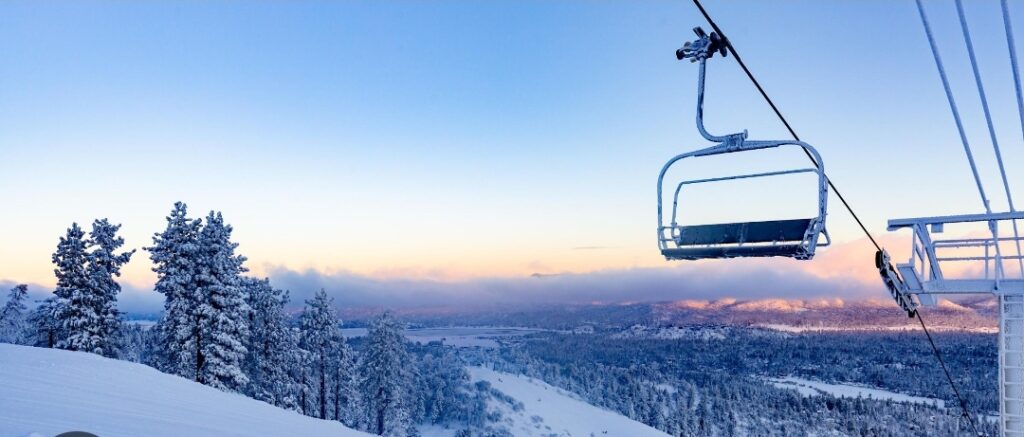 A ski lift with the sun setting over a snowy mountain.