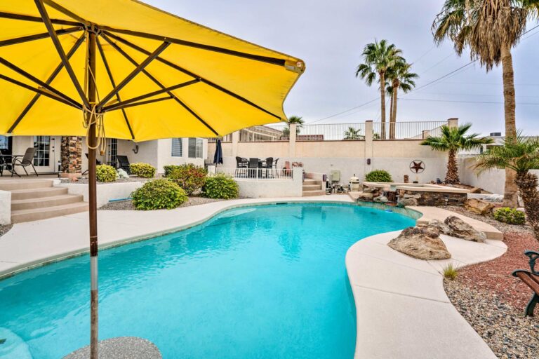 A pool with an umbrella and chairs in the back yard.